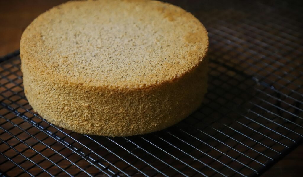 Freshly baked sponge cake resting on a wire cooling rack, perfect for desserts.