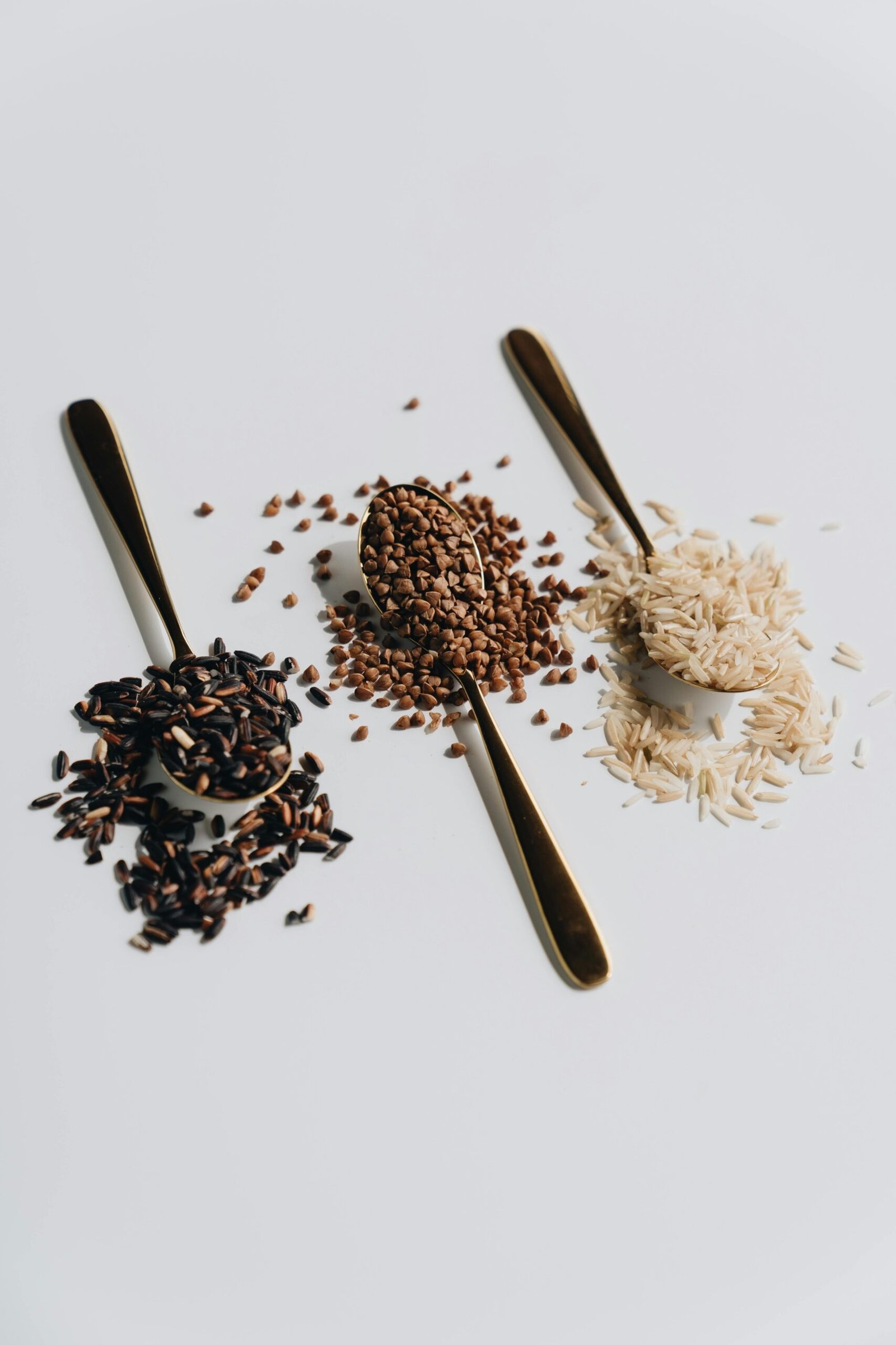 Three types of grains on spoons display variety on a white background, ideal for culinary themes.